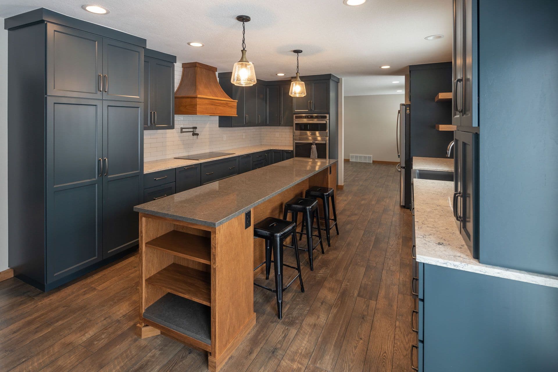A kitchen with dark gray-blue cabinets and a long central island with black bar stool seating.